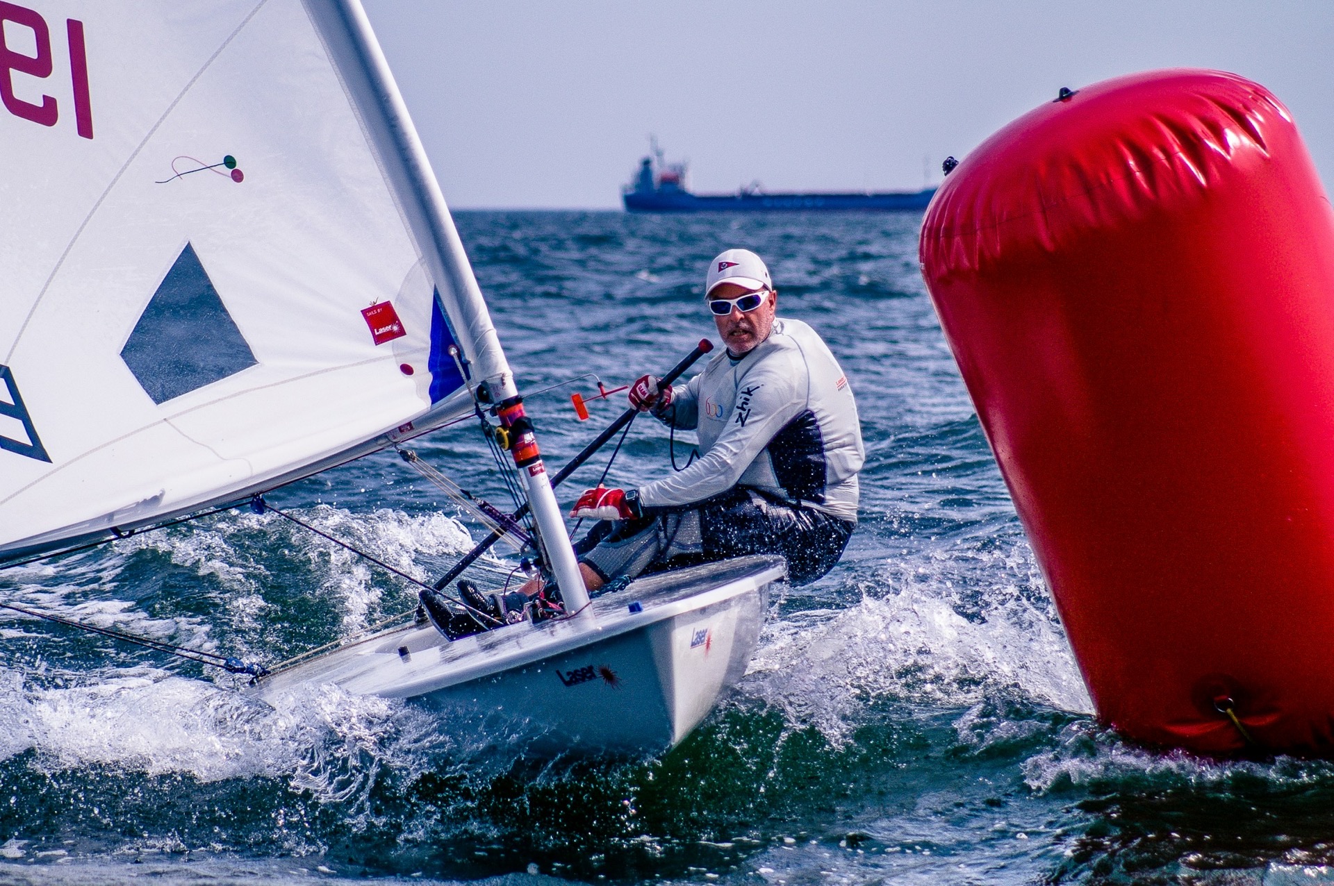 A Laser sailor rounding a red inflatable mark at speed